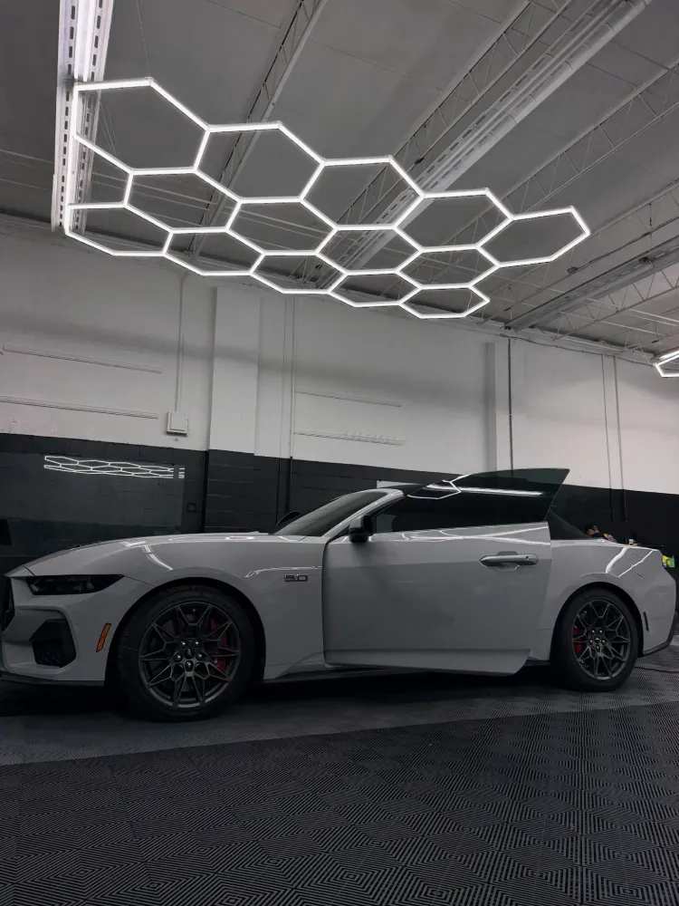 Side profile of a white sports car under shop lights before paint protection film removal