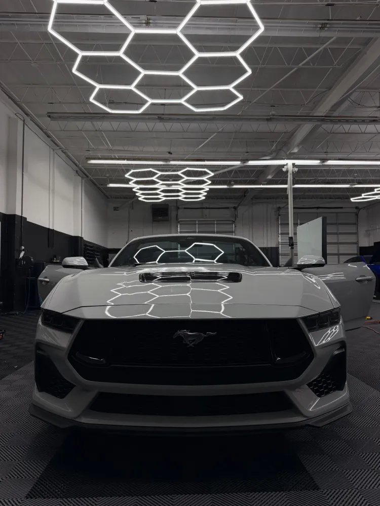 Front view of a white sports car receiving paint protection film service inside a shop